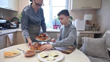 Kafkasyalı çocuk annesiyle evde hamburger pişiriyor.