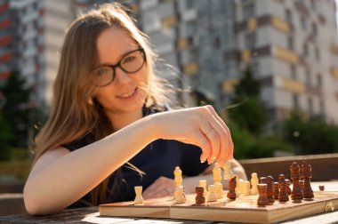 Beyaz kadın dışarıda satranç oynuyor.