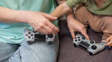 Beyaz kadın küçük oğluna konsol oynamayı öğretiyor. Oyun kolu ellerinde.