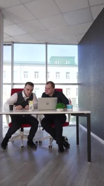 İki beyaz adam bir masada oturup iş tartışıyorlar.