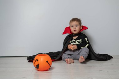 Beyaz arka planda şeker sepeti tutan Drakula kostümlü beyaz çocuk. Şaka mı şeker mi?