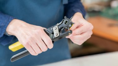 Bir kadın deri kemerde delikler açar. Deri işçileri atölyesi