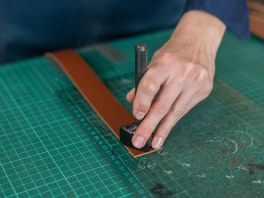 Kadın bronzlaştırıcı bir atölyede deri kemerin kenarlarını inceliyor.