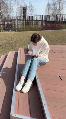 Açık havada kalemle çizim yapan beyaz bir kadın.