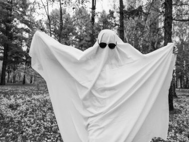 Bir sonbahar ormanının arka planında hayalet kostümlü bir kadın. Cadılar Bayramı kostümü. Siyah beyaz fotoğraf