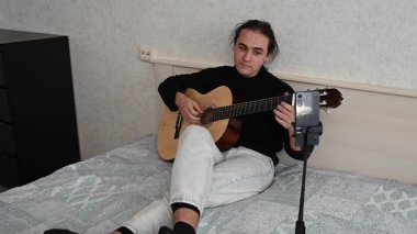 Genç adam kendini akıllı telefondan çekerken akustik gitar çalıyor. Parmak Biçimi