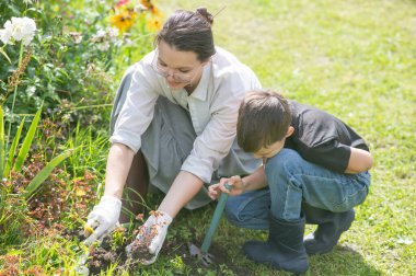 Beyaz kadın, oğullarıyla bahçesine bakıyor.