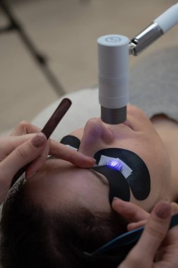 Kirpik uzatma prosedüründen geçen bir kadın ultraviyole lamba kullanıyor.