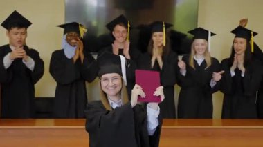 Sınıf arkadaşları onu alkışlarken, elinde diploma tutan beyaz bir kadın.