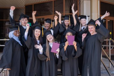 Farklı uluslardan mutlu öğrenciler mezuniyet elbiseleriyle diplomalarını tutuyorlar.