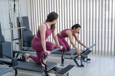 Pembe spor kıyafetli iki Asyalı kadın ıslah yatağıyla pilates egzersizi yapıyor.