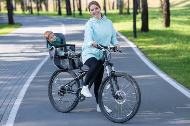 Küçük oğluyla bisiklete binen beyaz bir kadın arkasında çocuk koltuğunda oturuyor.