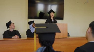 Genç bir kadın kürsüde duruyor ve sınıf arkadaşlarına mezuniyet konuşması yapıyor.