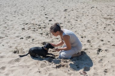 Beyaz bir kadın köpeğiyle sahilde yürüyor.