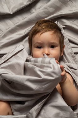 Beyaz tenli şirin bir çocuğun yatakta yatışının üst görüntüsü.