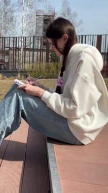 Açık havada kalemle çizim yapan beyaz bir kadın.