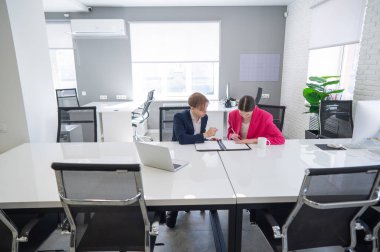 Kadın ve erkek ofiste otururken konuşuyorlar.