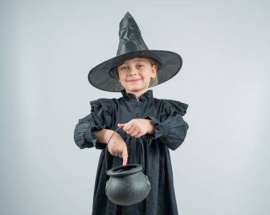 Beyaz arka planda bir kazan tutan cadı kostümlü beyaz bir kızın portresi.