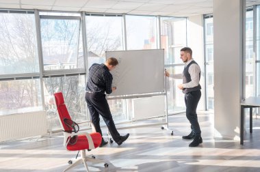 Beyaz bir kurulda iş tartışan iki beyaz adam.