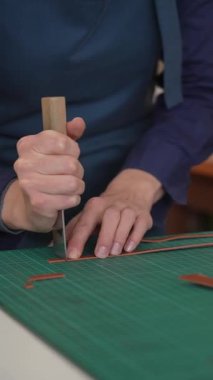 Deri işçisi bir atölyedeki kemerden bir parça deri kesiyor.