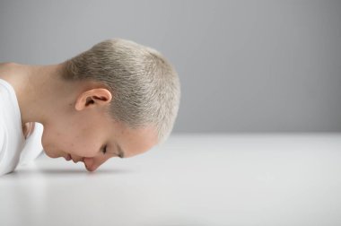 Üzgün bir kadın beyaz bir arka planda, kafası masanın üzerinde oturuyor.