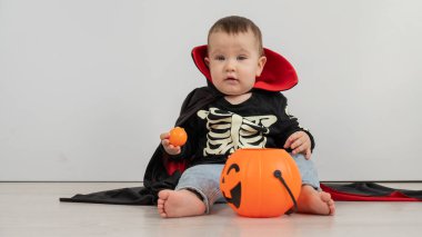 Beyaz arka planda şeker sepeti tutan Dracula Cadılar Bayramı kostümlü beyaz tatlı çocuk.