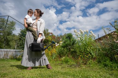 Beyaz kadın ve oğlu bahçede çiçek suluyorlar.