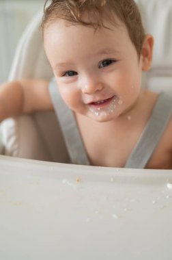 Ekşi kremaya bulanmış sevimli erkek bebek yüksek bir sandalyede oturuyor.