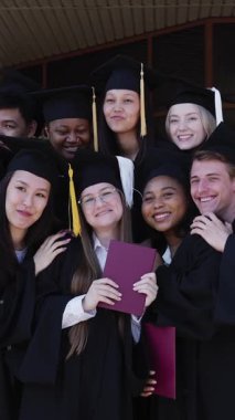 Farklı uluslardan mutlu öğrenciler mezuniyet elbiseleriyle diplomalarını tutuyorlar.