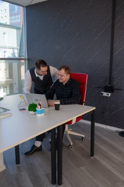 Beyaz adam çalışma masasında durmuş iş hakkında konuşuyor.