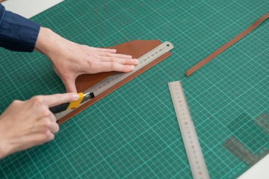 Deri işçisi atölyede deri kesip ölçüyor.