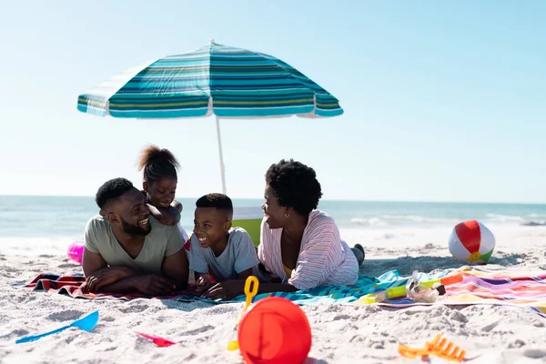 幸せなアフリカ系アメリカ人の両親と子供たちは 空の下で砂浜のタオルに横になって話しています コピースペース 変更されていない 一緒に パラソル ピクニック 楽しみと夏 — ストック写真