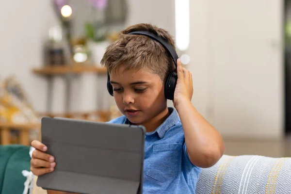 白人男孩坐在客厅沙发上 头戴耳机 使用数码平板电脑 不变的生活方式 技术和家庭观念 — 图库照片