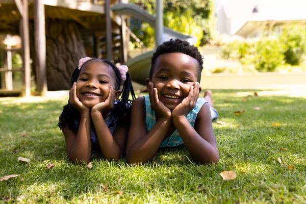 一个可爱的非洲裔美国兄弟姐妹的肖像 手牵着下巴躺在公园的草地上 不变的 家庭的 团聚的 童年的 微笑的 快乐的和周末的观念 — 图库照片