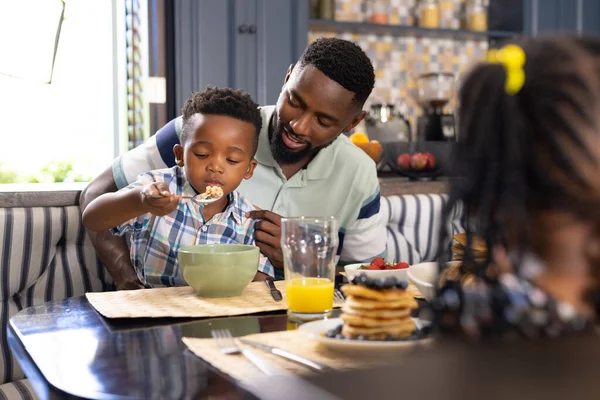 美国黑人父亲看着儿子在家里的饭桌上吃早餐谷类食品 抄袭空间 生活方式 新鲜健康的概念 — 图库照片