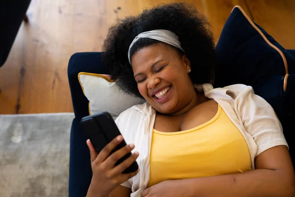 Счастливая Афроамериканка Плюс Размер Лежащая Диване Помощью Смартфона Смеющаяся Расслабление — стоковое фото