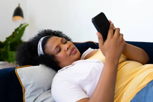 幸せプラスサイズアフリカ系アメリカ人女性ソファに横たわって スマートフォンを使用しています リラクゼーション コミュニケーション 家庭生活 身体的包容力とライフスタイル 変わらない — ストック写真