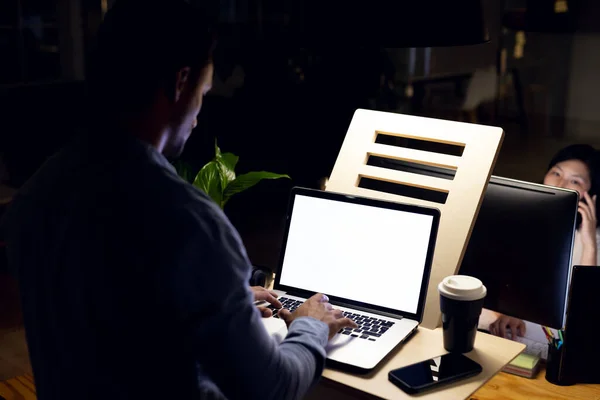 Biracial businessman standing at desk using laptop with copy space on screen, working late at office. Business, overtime, work, communication and technology.