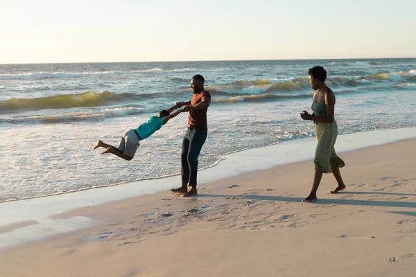Африканская Американка Смотрит Игривого Мужа Крутящего Своего Сына Пляже Время — стоковое фото