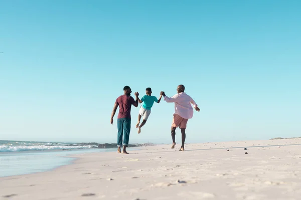ビーチで遊んでいる大人の息子と孫と幸せなアフリカ系アメリカ人の祖父 家族と休暇 — ストック写真