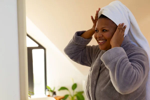 快乐又大的非洲女人穿着长袍 在浴室的镜子里看着自己 自我照顾 健康和美 身体包容和生活方式 — 图库照片
