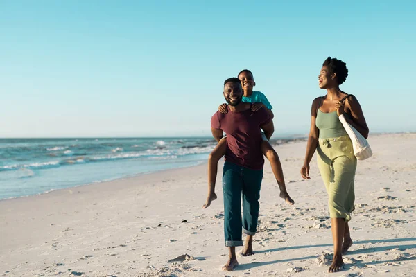 幸せなアフリカ系アメリカ人の女性が夫と一緒に空に対してビーチで子豚バッキング コピースペースを歩いている 変更されない 一緒に 子供時代 楽しみと夏の概念 — ストック写真