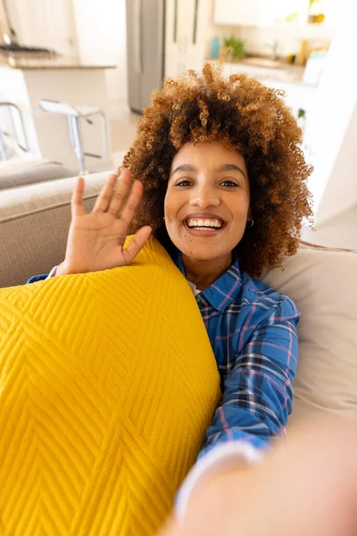 ソファの上でクッションで休んでいる間に手を振ってアフロ髪の幸せな出産の若い女性の肖像画 変更されていない ジェスチャー ライフスタイル 黄色と家のコンセプト — ストック写真