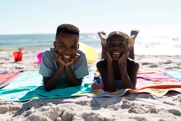 アフリカ系アメリカ人の幸せな兄弟の肖像画の手にあごの上にタオルの上に横たわって空に対してビーチ コピースペース 変更されていない 子供時代 ピクニック リラックス 楽しさと夏 — ストック写真