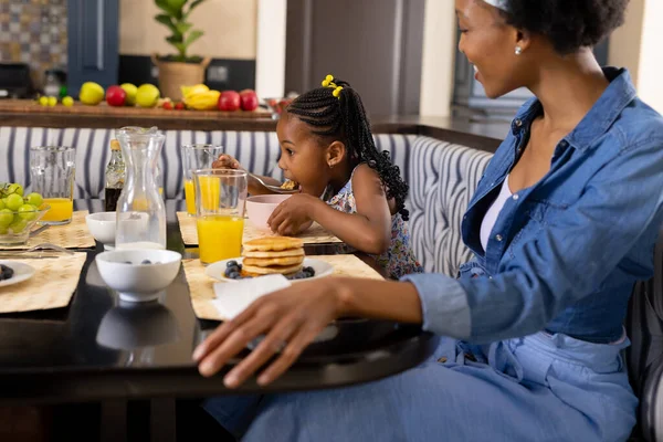 非洲裔美国母亲看着女儿在家里的餐桌边吃着煎饼和果汁 不变的家庭 新鲜和生活方式概念 — 图库照片