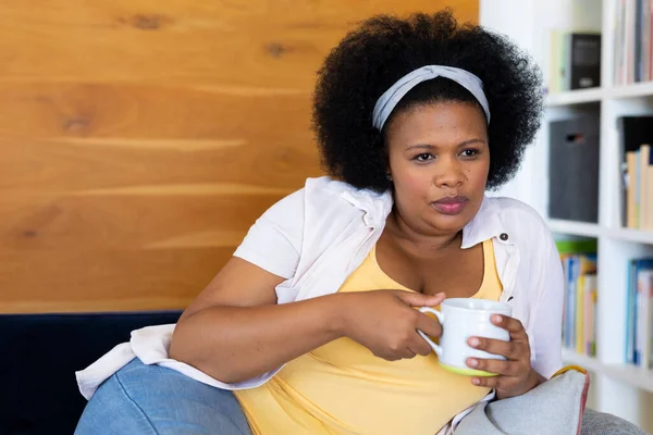有思想的加体形的非洲裔美国女人躺在沙发上抱着杯子放松 闲暇时间 家庭生活 身体包容和生活方式 — 图库照片