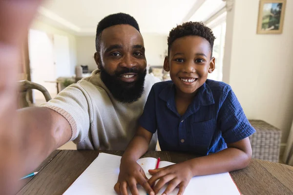快乐的非洲裔美国父亲和儿子坐在桌旁 带着笔记本和视频通话 视频通话 家庭和家庭生活 — 图库照片