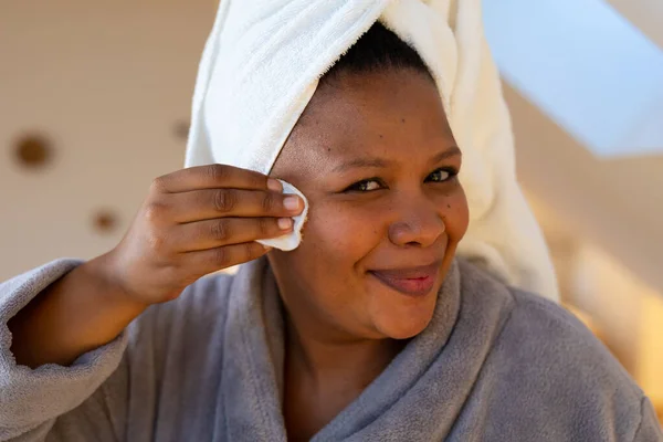 快乐加尺寸的非洲女人穿着长袍 洗脸用棉垫在浴室里 自我照顾 健康和美 身体包容和生活方式 — 图库照片