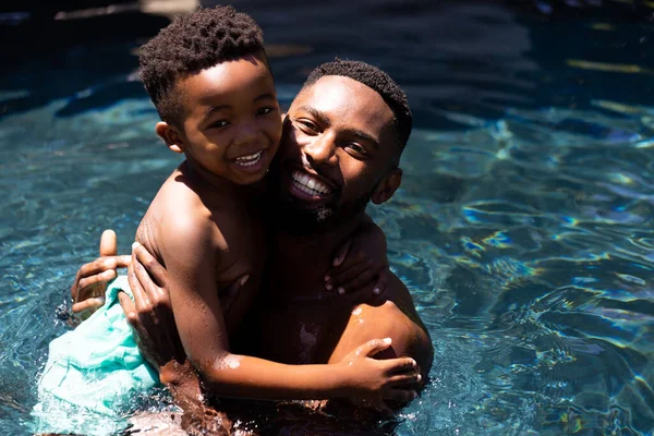 一个快乐的非洲裔美国父亲在度假胜地的游泳池里抱着儿子的画像 不变的家庭 夏天和周末的概念 — 图库照片