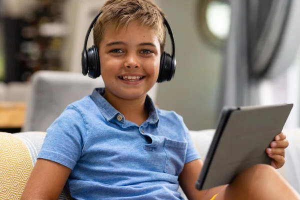 坐在沙发上的白人男孩头戴耳机 使用数码平板电脑的肖像 不变的生活方式 科技和家庭观念 — 图库照片